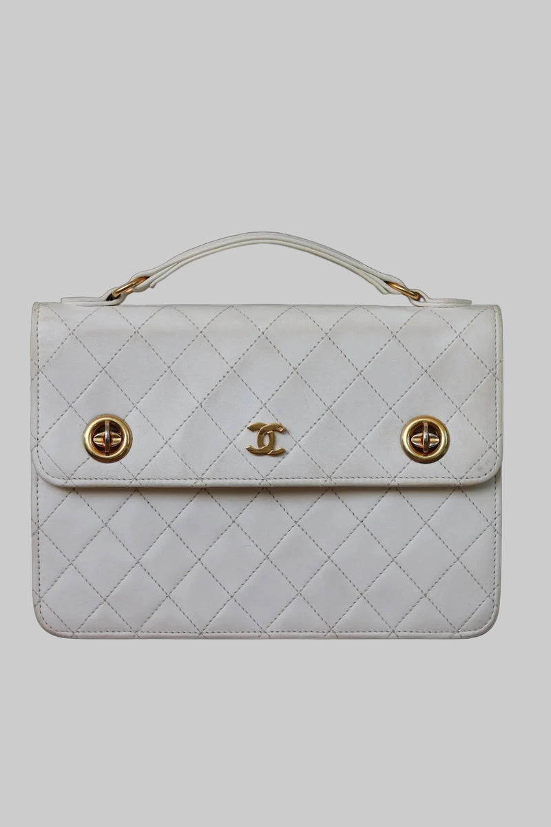 Front view of a vintage Chanel small briefcase in white quilted lambskin with gold-tone double turnlocks and a top handle
